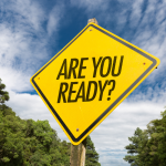 picture of yellow sign with phrase "Are You Ready?" in the middle in all capital letters. Background is a photo of a cloudy blue sky and trees.